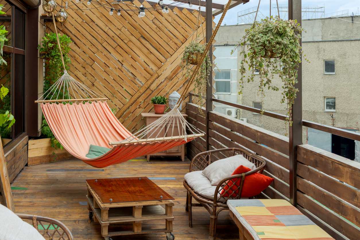 A balcony with a hammock, hanging plants, and mismatched furniture.