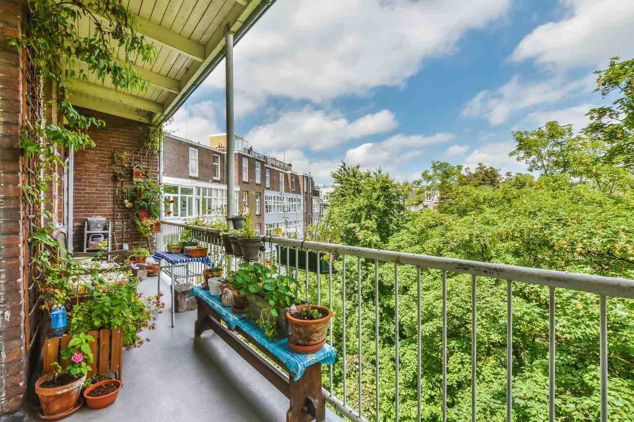 An apartment balcony filled with lush green plants, with a potting bench, plant stand, and table.