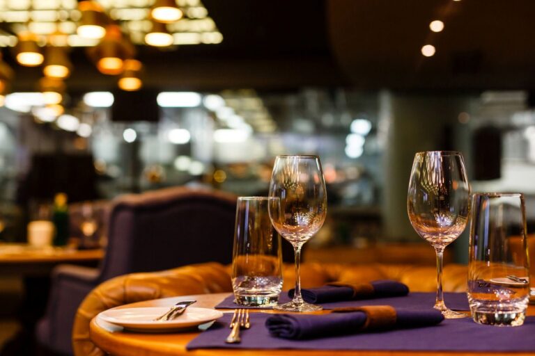 A table in a fine dining restaurant with utensils, plates, glass cups, and wine glasses against a blurred background