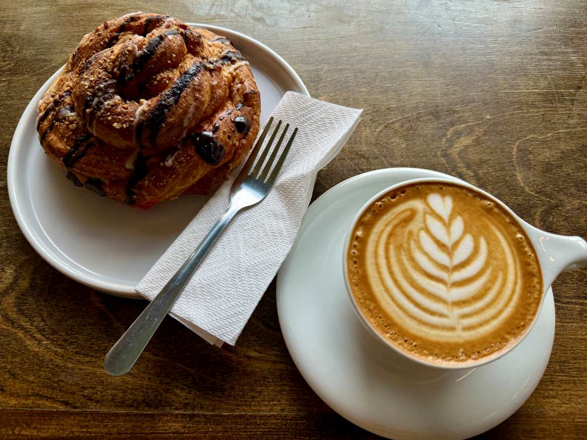 A latte with an artful design next to a plated pastry