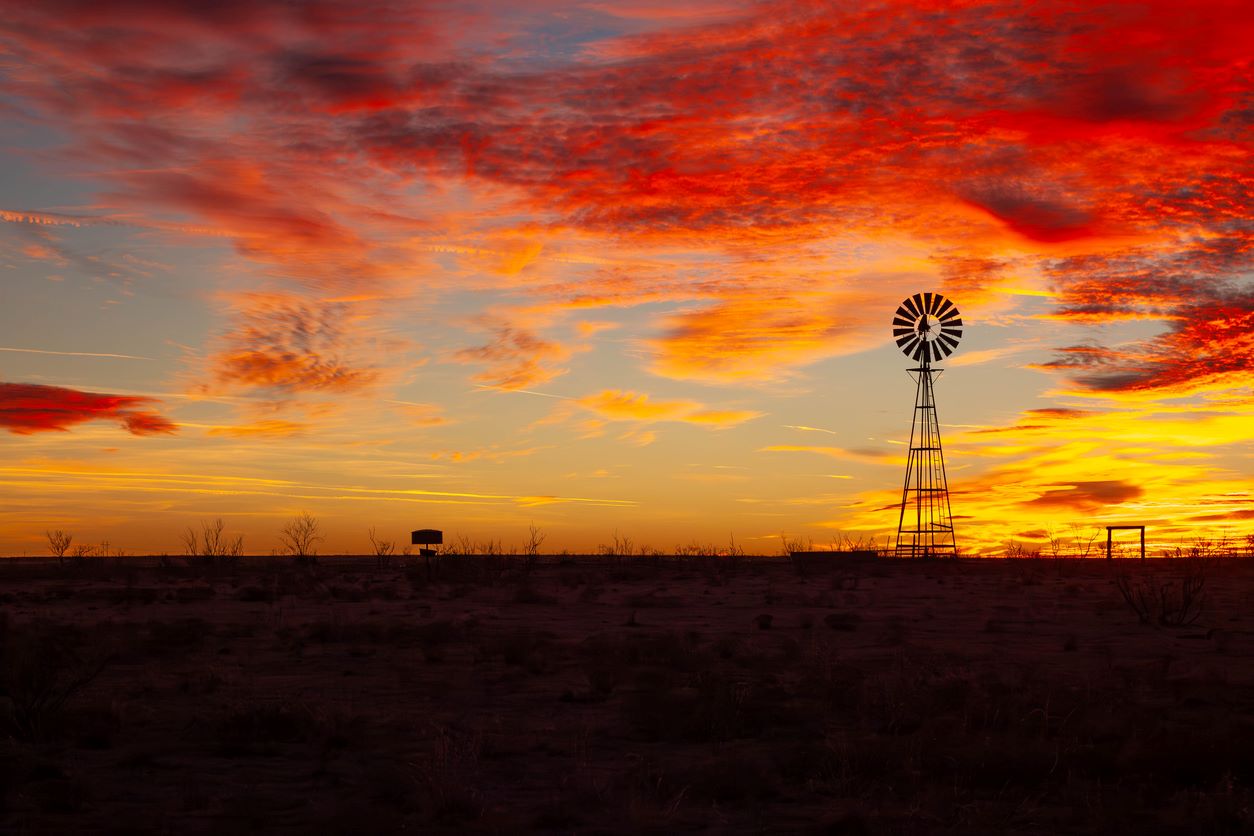 The sunset over a field in Amarillo with a windmill in the distance