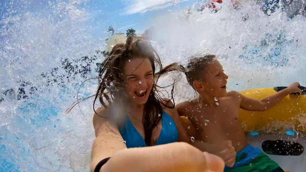 Woman and boy laughing while riding a water slide